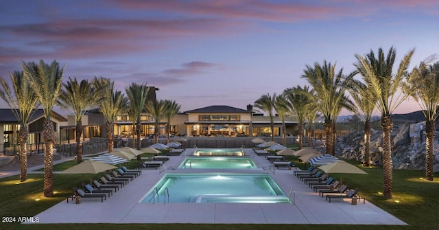 pool at dusk featuring a patio, a lawn, and a community hot tub