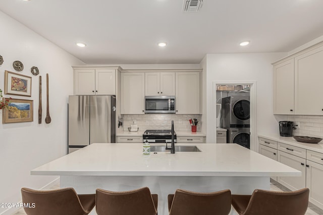 kitchen featuring a center island with sink, stainless steel appliances, backsplash, and stacked washing maching and dryer