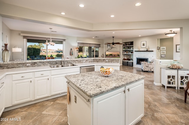 kitchen featuring sink, a kitchen island, a brick fireplace, hanging light fixtures, and white cabinetry