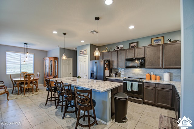 kitchen with light stone countertops, appliances with stainless steel finishes, decorative light fixtures, backsplash, and an island with sink