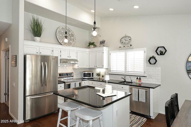 kitchen with decorative backsplash, white cabinets, under cabinet range hood, appliances with stainless steel finishes, and dark countertops