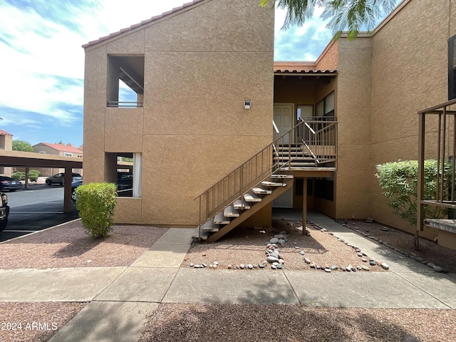 exterior space with stucco siding, covered parking, stairs, and a tiled roof