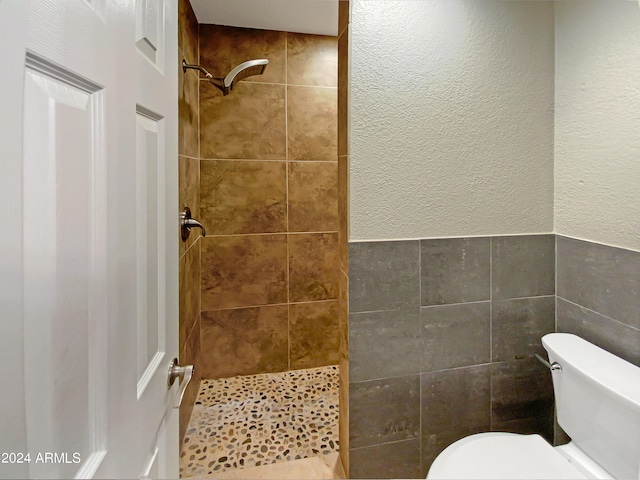 bathroom with tile walls, toilet, a textured wall, and tiled shower