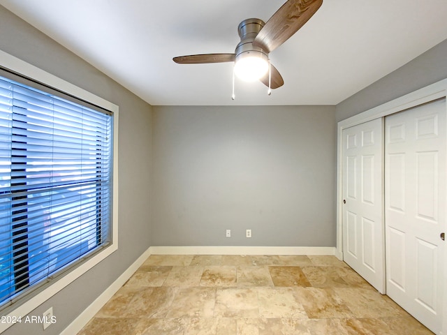 unfurnished bedroom with multiple windows, a ceiling fan, baseboards, and a closet