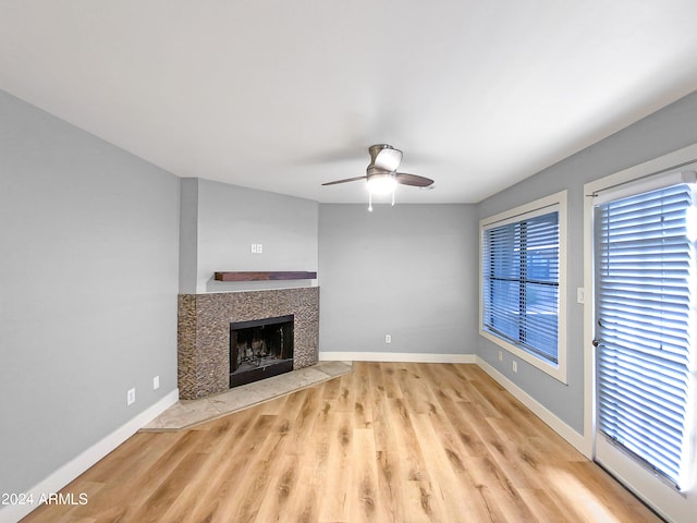 unfurnished living room with ceiling fan, light wood-style floors, baseboards, and a tile fireplace