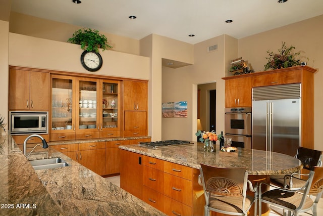 kitchen featuring built in appliances, sink, light stone countertops, and a kitchen bar