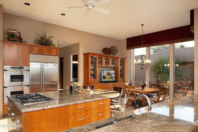 kitchen featuring light stone counters, stainless steel appliances, decorative light fixtures, and ceiling fan with notable chandelier