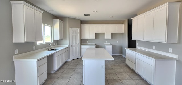 kitchen with light tile floors, white cabinets, a kitchen island, and sink