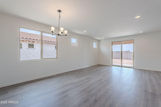 unfurnished room featuring wood finished floors, an inviting chandelier, visible vents, and a wealth of natural light