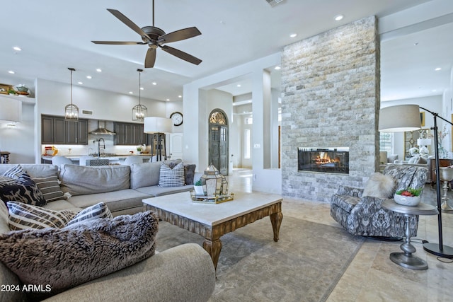 living room featuring ceiling fan, a stone fireplace, and sink