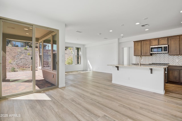 4053 Desert Moon Dr, Wickenburg, AZ 85390 - kitchen with stainless steel microwave, decorative backsplash, recessed lighting, a kitchen island with sink, and light wood-type flooring