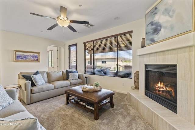 living room with carpet floors, a tiled fireplace, a ceiling fan, baseboards, and visible vents