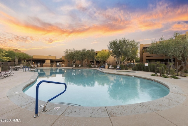 pool at dusk with a community pool, a patio, a hot tub, and fence