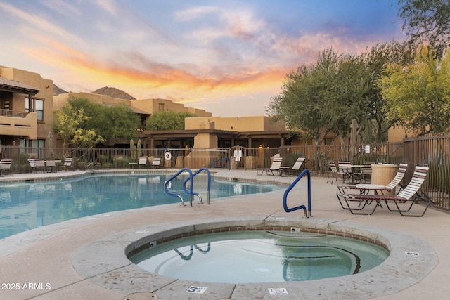 pool at dusk with fence, a patio, and a community hot tub