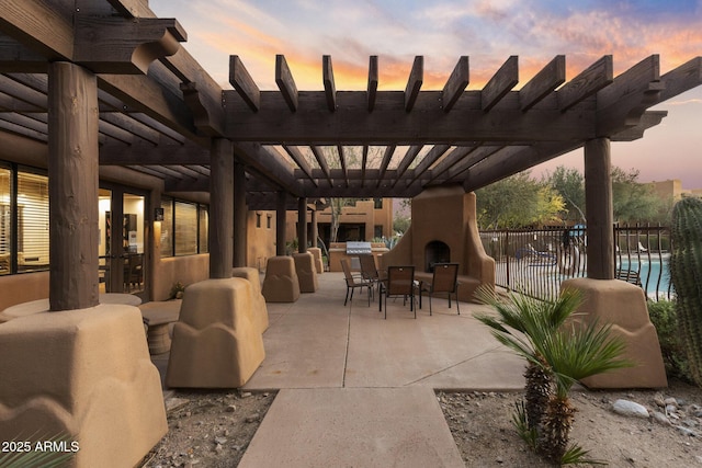 patio terrace at dusk featuring fence, a pergola, outdoor dining space, and a large fireplace