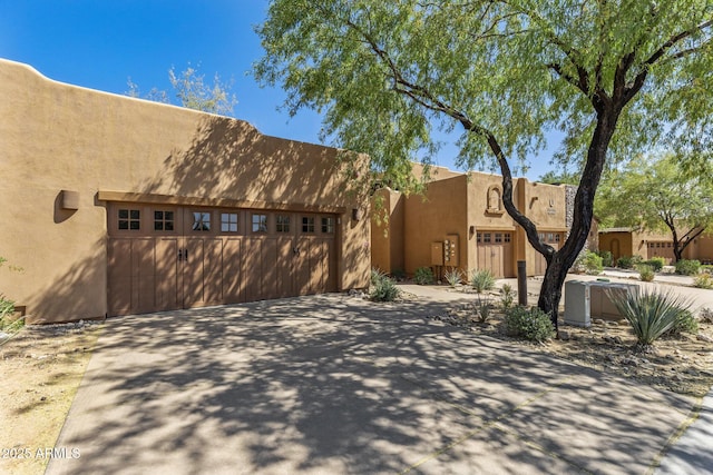 adobe home featuring a garage, stucco siding, and concrete driveway