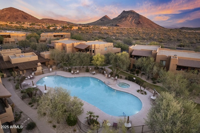 pool at dusk featuring fence, a mountain view, a community pool, and a hot tub