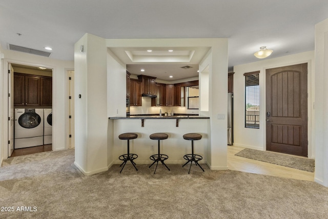 kitchen featuring visible vents, washer and dryer, a kitchen breakfast bar, light colored carpet, and a tray ceiling