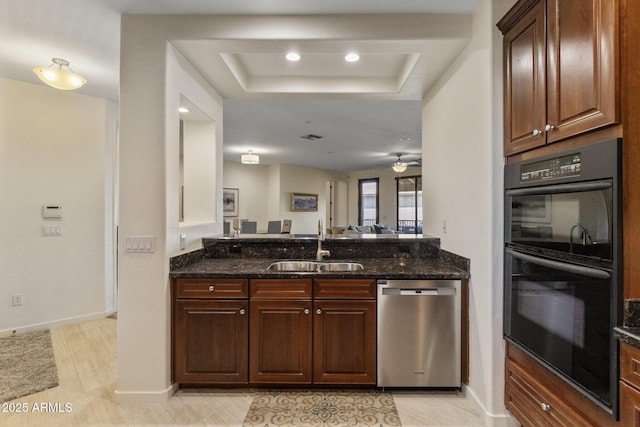 kitchen with a sink, a raised ceiling, dishwasher, dobule oven black, and dark stone countertops