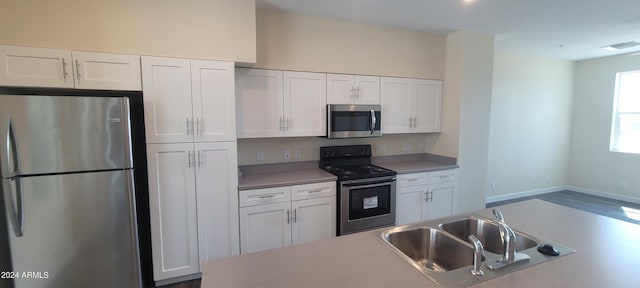 kitchen with light countertops, appliances with stainless steel finishes, white cabinetry, a sink, and baseboards