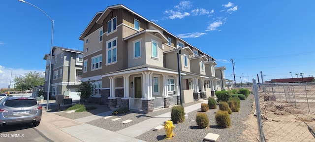 view of front of house featuring a residential view, covered porch, fence, and stucco siding