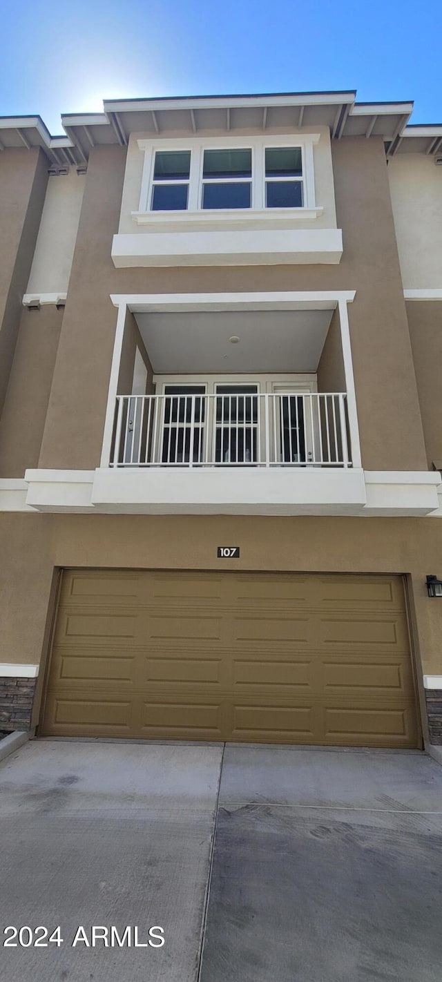 view of property with driveway, a balcony, an attached garage, and stucco siding