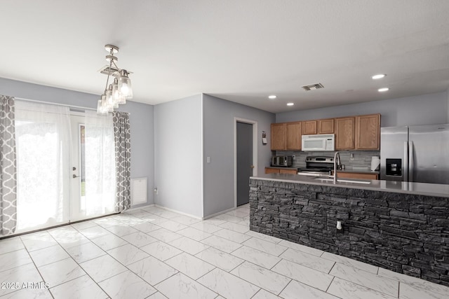 kitchen with backsplash, stainless steel appliances, a sink, decorative light fixtures, and brown cabinetry