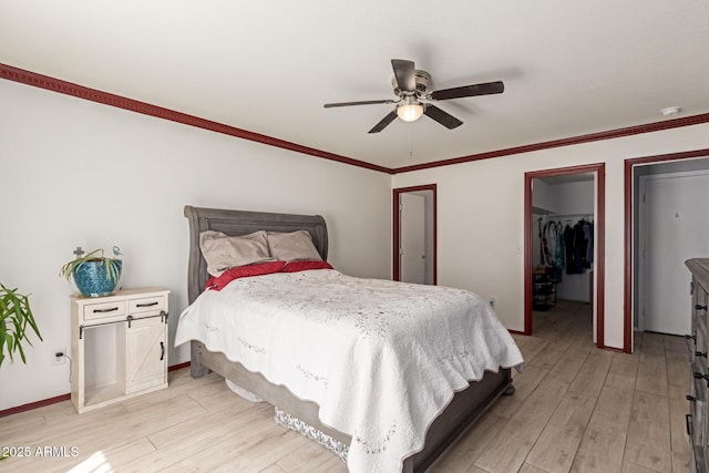 bedroom with a walk in closet, baseboards, light wood-type flooring, and ornamental molding