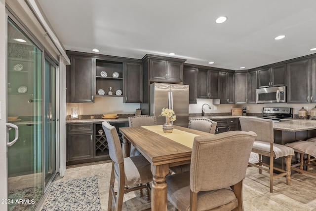 kitchen featuring a kitchen island, dark brown cabinets, stainless steel appliances, light stone counters, and a breakfast bar