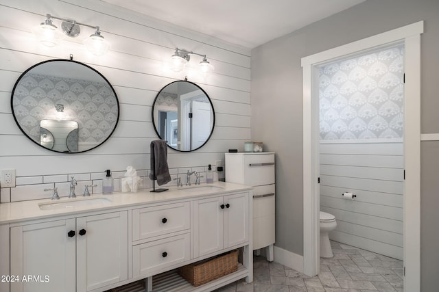 bathroom featuring a sink, wood walls, toilet, and double vanity