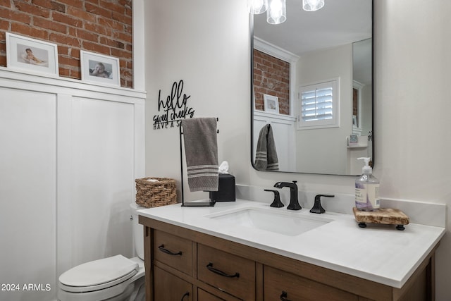 bathroom featuring brick wall, vanity, and toilet