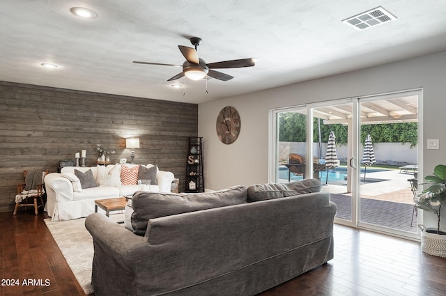 living room featuring wood walls, ceiling fan, visible vents, and wood finished floors