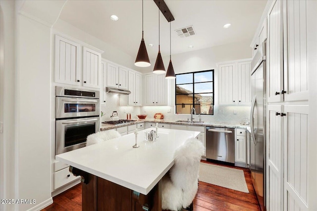 kitchen with sink, white cabinetry, stainless steel appliances, a center island, and decorative light fixtures