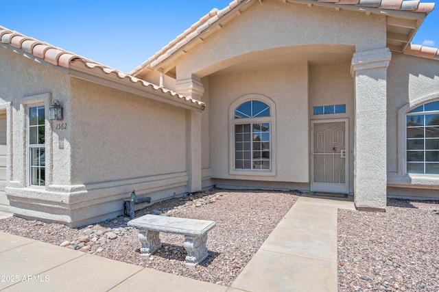 view of exterior entry with stucco siding and a tiled roof