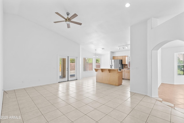 unfurnished living room with arched walkways, ceiling fan, light tile patterned floors, and a healthy amount of sunlight