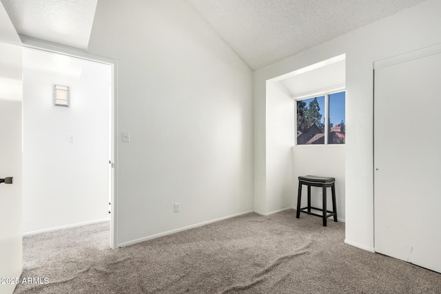 unfurnished room featuring a textured ceiling, carpet, and vaulted ceiling