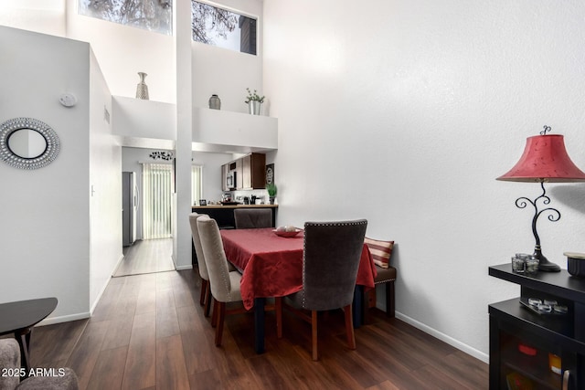 dining space featuring a towering ceiling and dark wood-type flooring