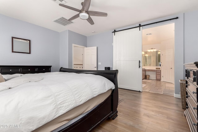 20409 W Thayer St, Buckeye, AZ 85396 - bedroom featuring a barn door, wood finished floors, connected bathroom, and ceiling fan