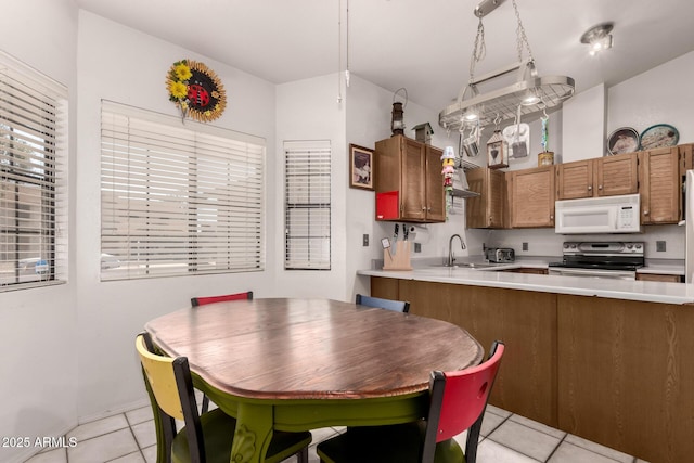 kitchen featuring white microwave, stainless steel electric range oven, light tile patterned floors, a sink, and light countertops