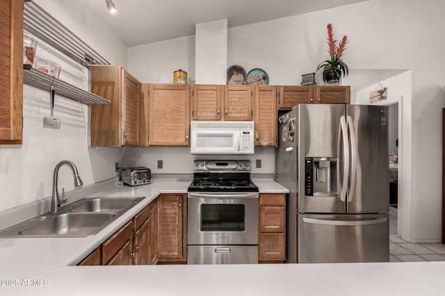 kitchen with stainless steel appliances, a sink, light countertops, light tile patterned flooring, and brown cabinetry