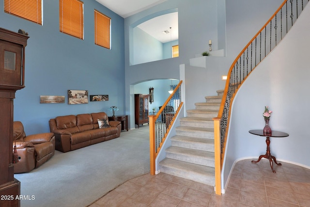 stairs featuring a towering ceiling, carpet, arched walkways, and tile patterned floors