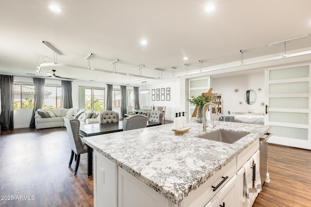 kitchen with white cabinets, open floor plan, light stone countertops, a kitchen island with sink, and a sink