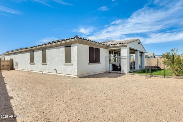 rear view of house featuring a tiled roof, fence, and stucco siding