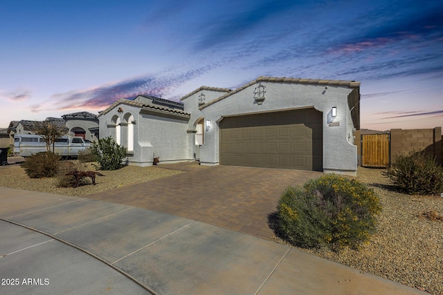 mediterranean / spanish-style home with decorative driveway, a tile roof, stucco siding, an attached garage, and fence