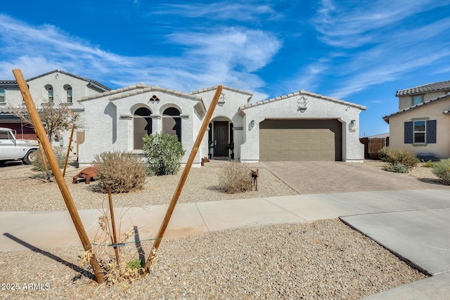 mediterranean / spanish home featuring a garage, a tile roof, decorative driveway, and stucco siding