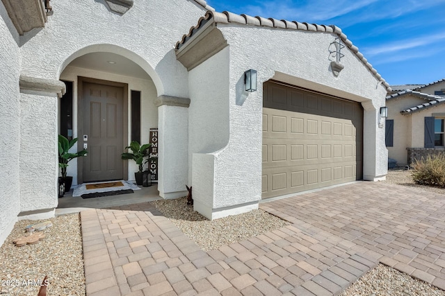 doorway to property featuring a garage, decorative driveway, a tile roof, and stucco siding