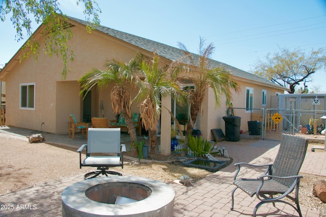 rear view of house featuring a patio area, stucco siding, an outdoor fire pit, and a gate