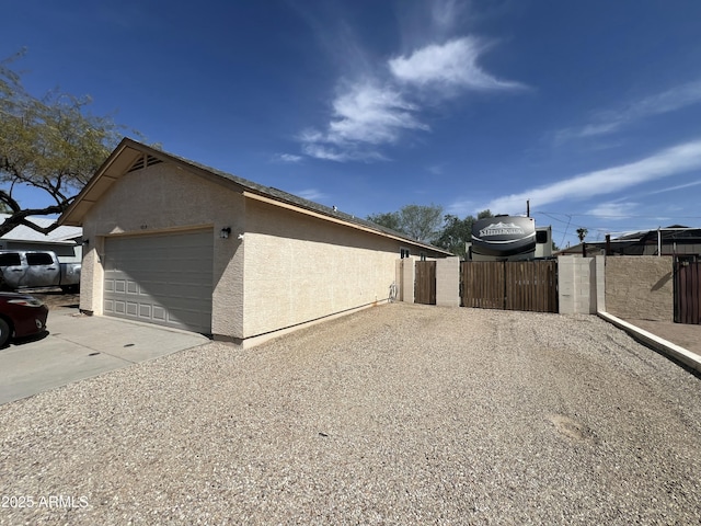 view of side of property with stucco siding, concrete driveway, fence, and a gate