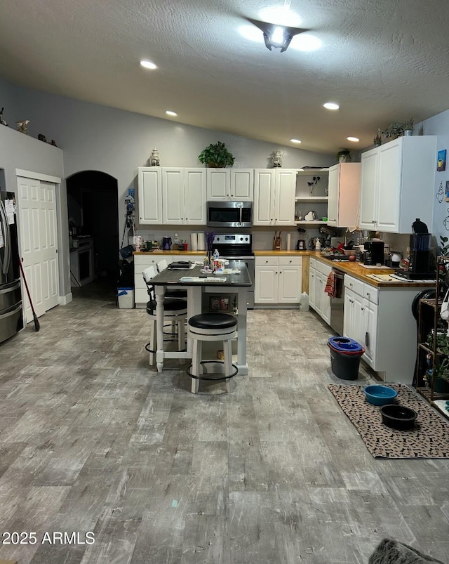 kitchen featuring a sink, stainless steel appliances, light wood-style floors, white cabinets, and vaulted ceiling