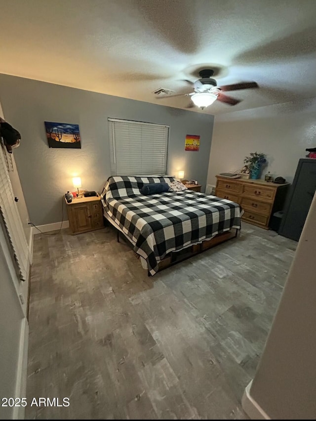 bedroom with visible vents, a textured ceiling, wood finished floors, baseboards, and ceiling fan